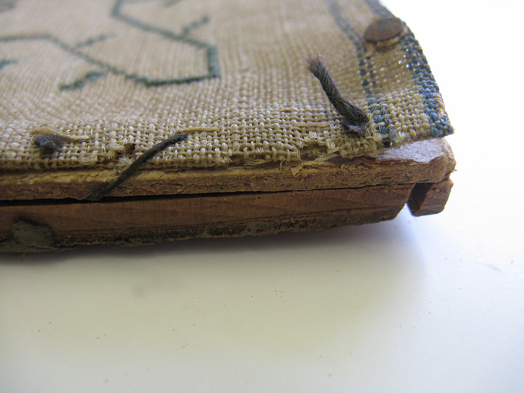 A detail of the previous stitching of the sampler onto the old mounting board.