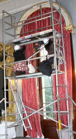 Conservators working at height on the top half of a pair of curtains.